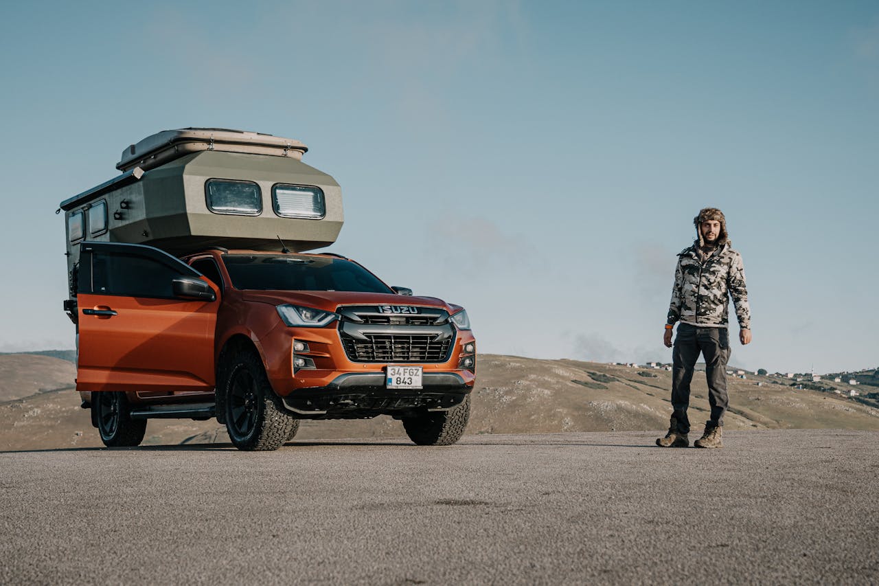 about-02 Man standing by an orange SUV with camper cabin in Ordu, Türkiye's scenic hills.